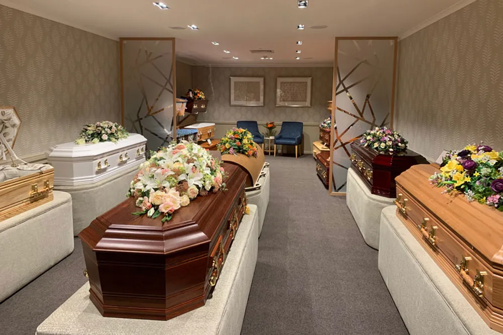 Several coffins adorned with floral arrangements in a viewing room.