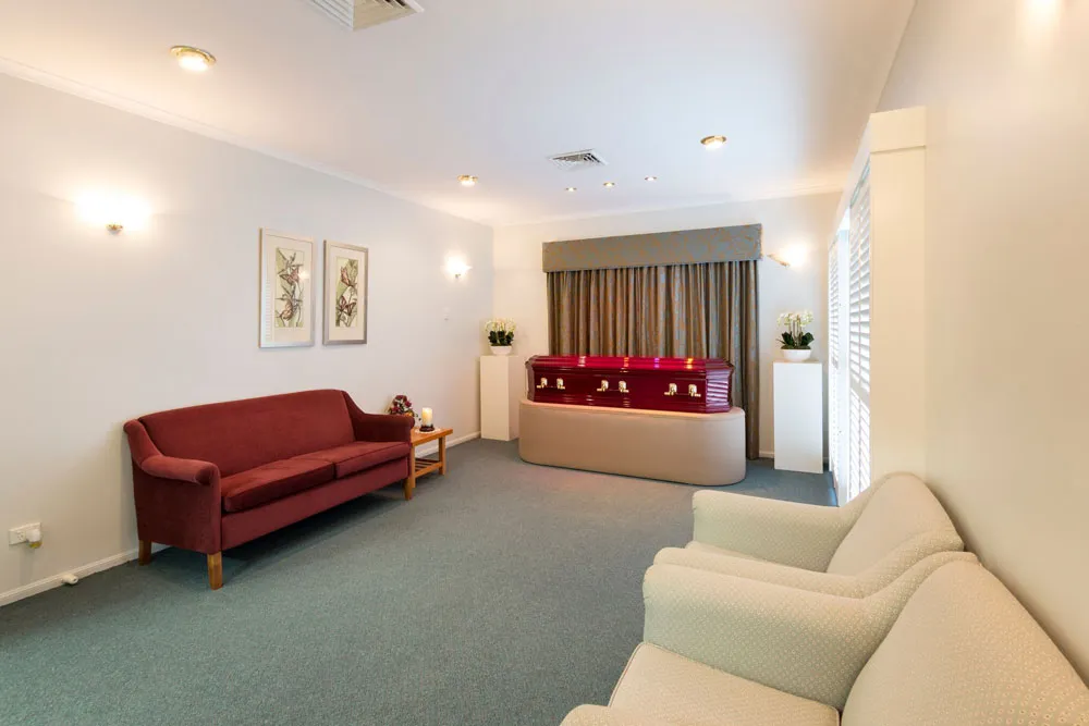 Red coffin in a peaceful, well-lit viewing room with seating.