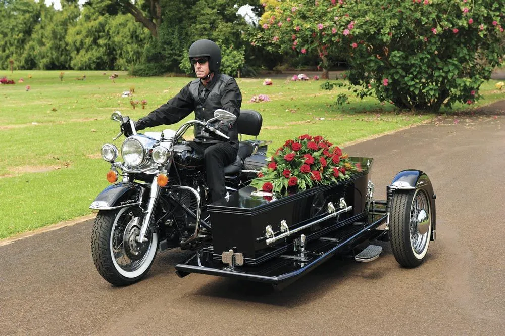 Motorcycle hearse with a rider and flowers.