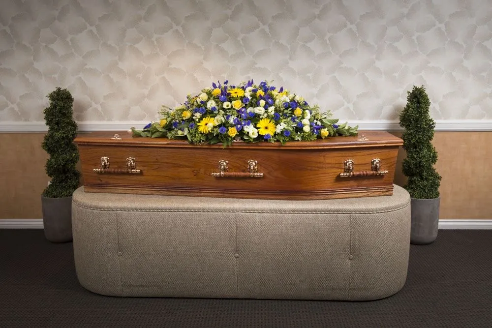 Ornate casket with yellow and purple flowers in viewing room.