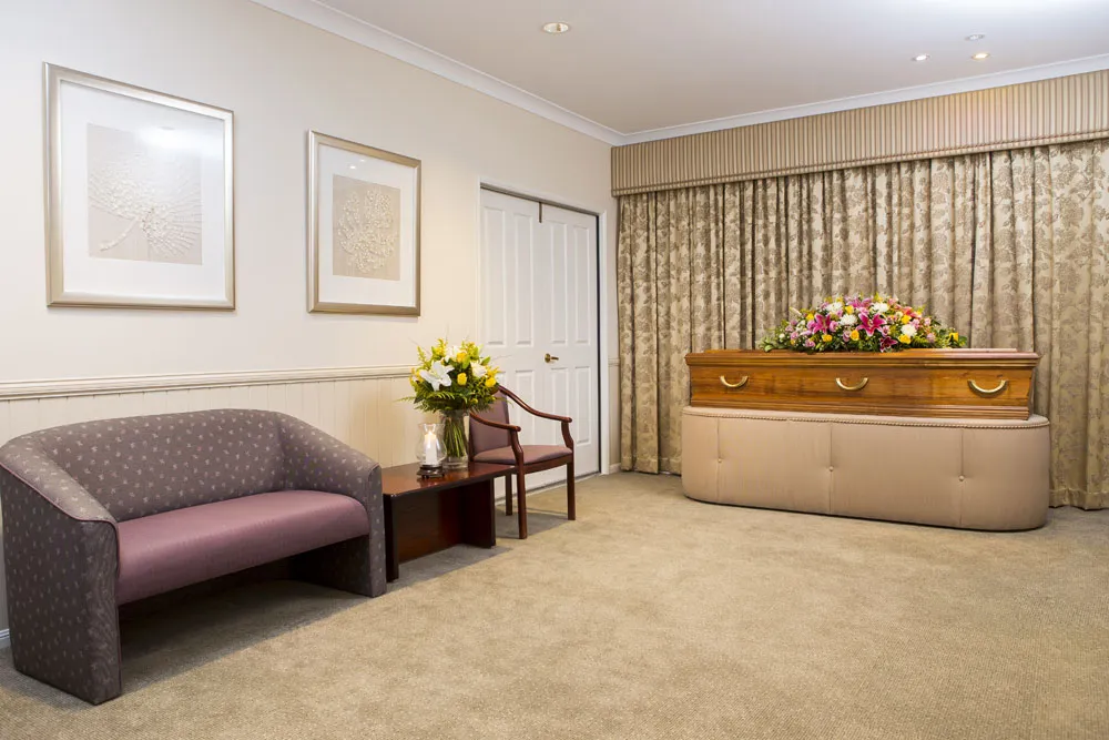 Purple sofa and casket with flowers in a warm viewing room.