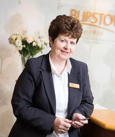 Woman in suit with nametag standing at a desk smiling.