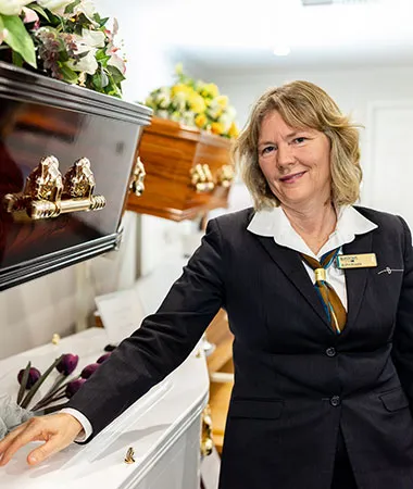 Funeral director standing among caskets with flowers.