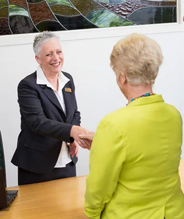 Two women shaking hands at a reception desk.