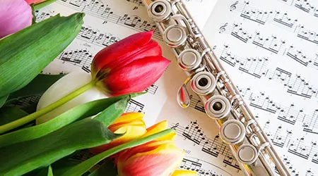 A silver flute and colorful tulips on a sheet of music.
