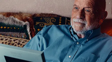 A thoughtful elderly man holds a framed photo or memorial item.