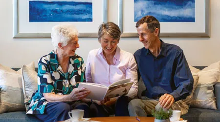 Three people smiling and looking at a book together.