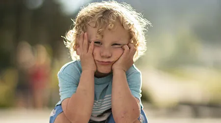 A bored-looking boy with curly hair rests his face in his hands.