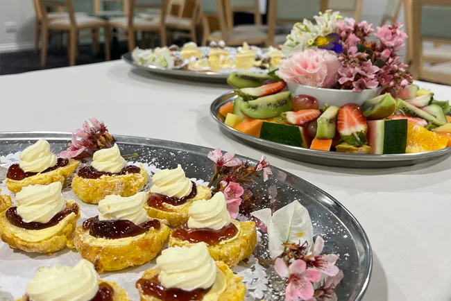 A table with three silver platters of food. The foreground platter has small pastries with cream and jam.