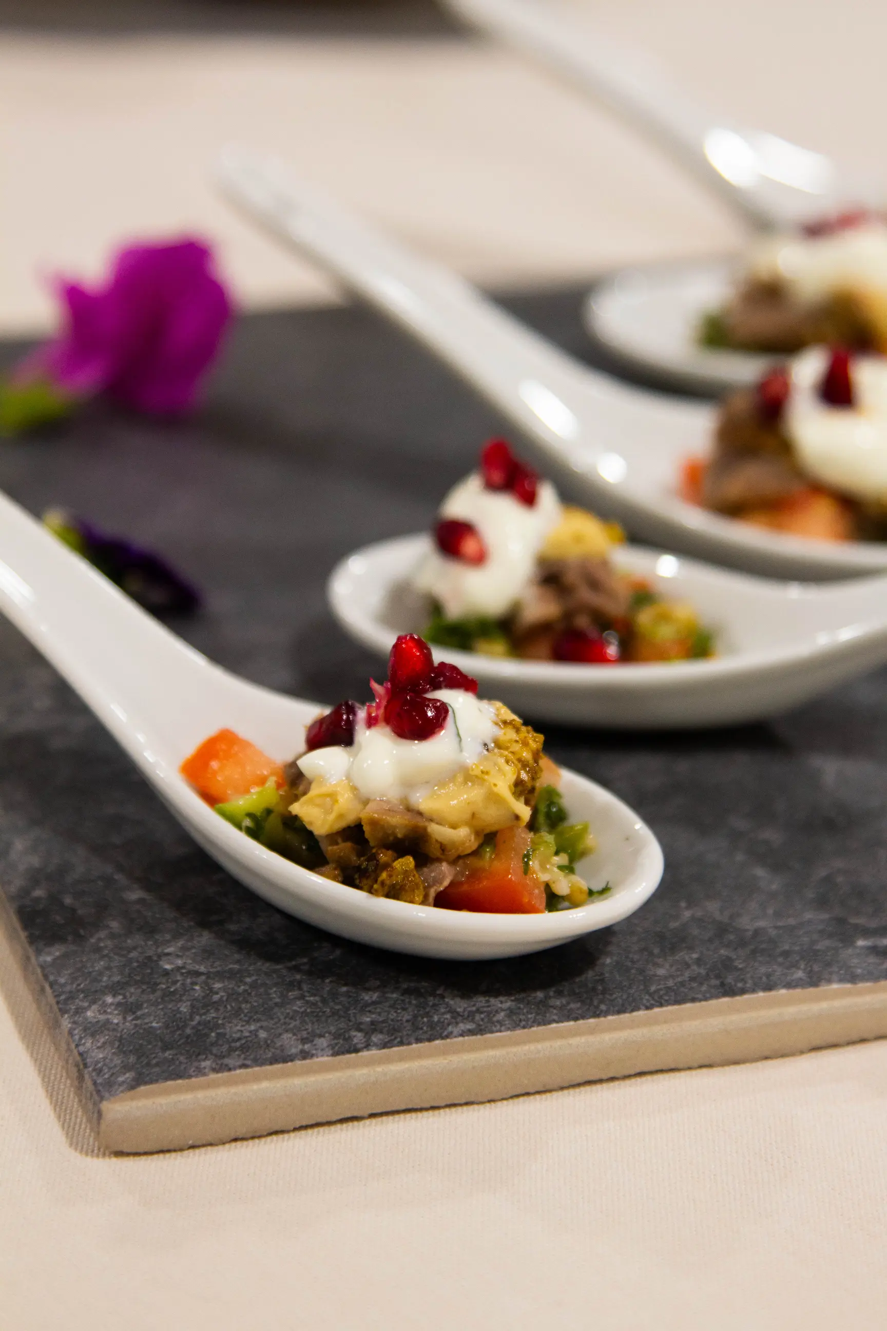 Gourmet appetizers topped with cream and pomegranate seeds served on ceramic spoons.