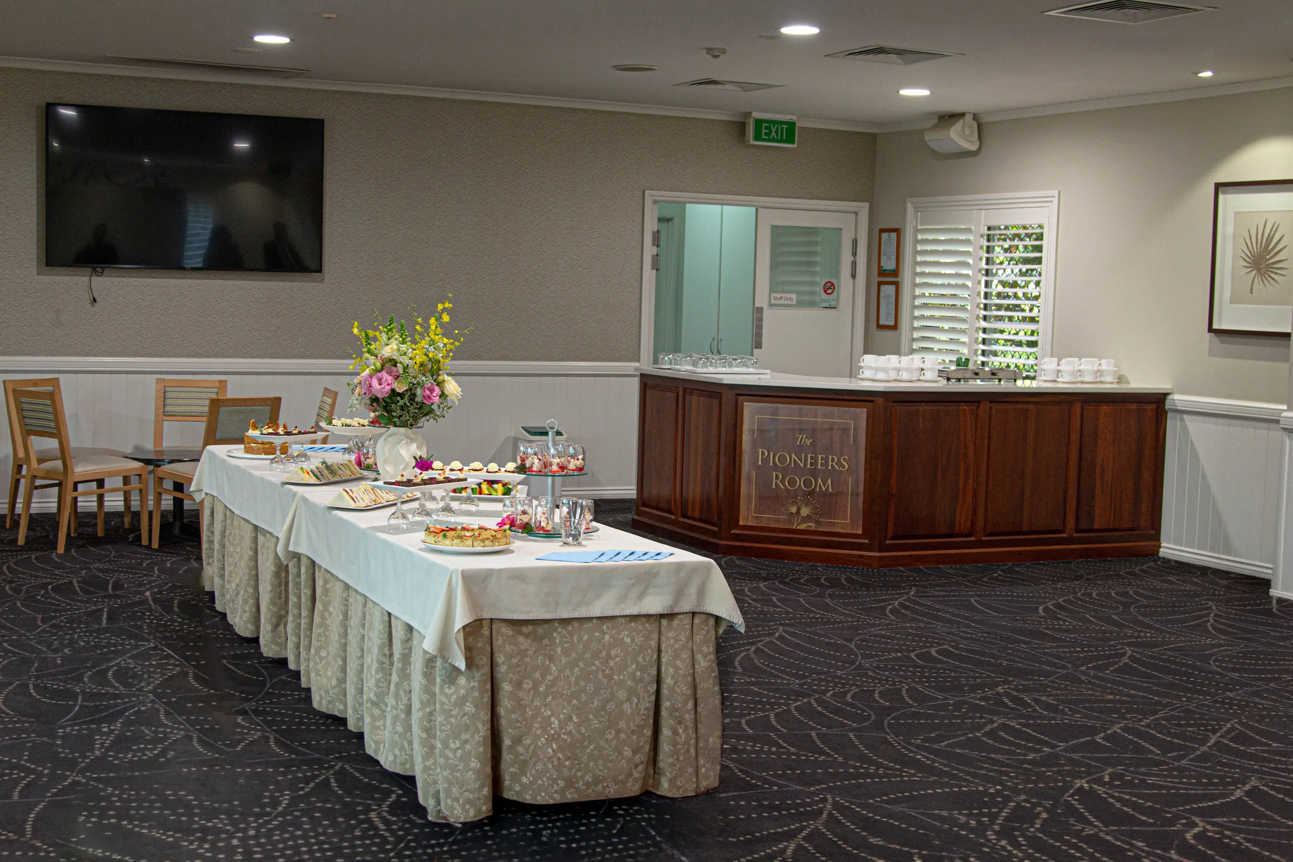Long buffet table set with flowers and food in front of a wooden counter bar.