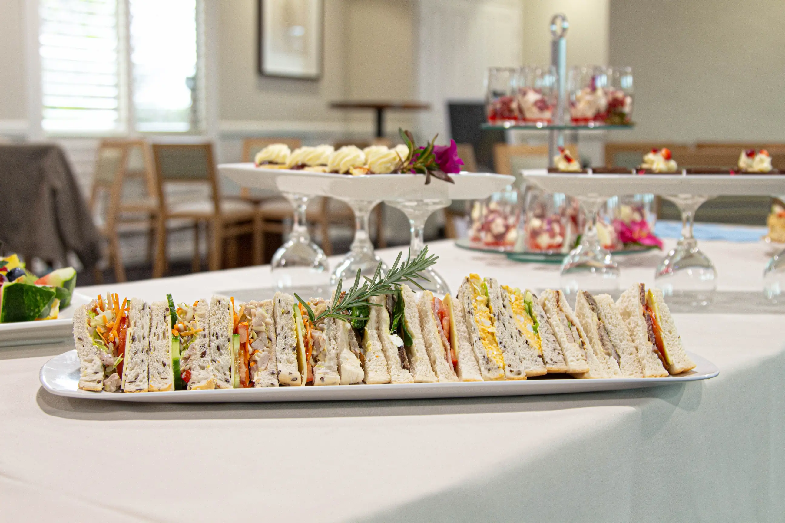 Platter of assorted tea sandwiches lined up on a white table covering for event catering.