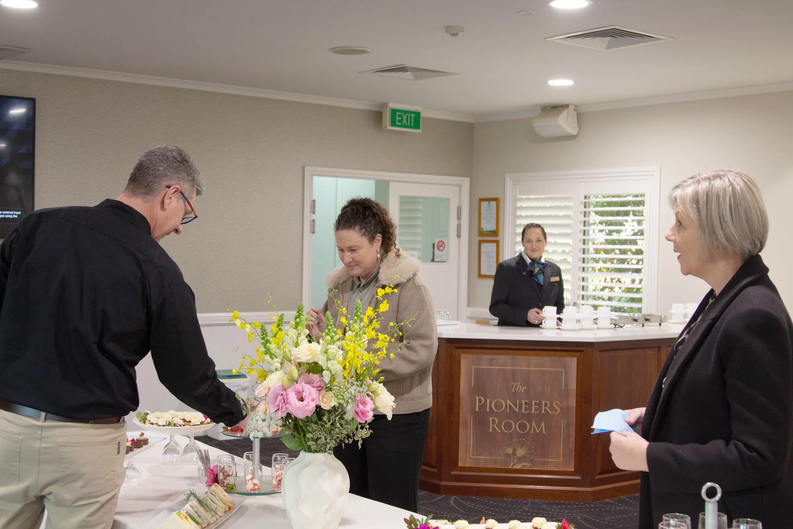 Guests browsing a catered food table inside a modern event lounge with staff nearby.