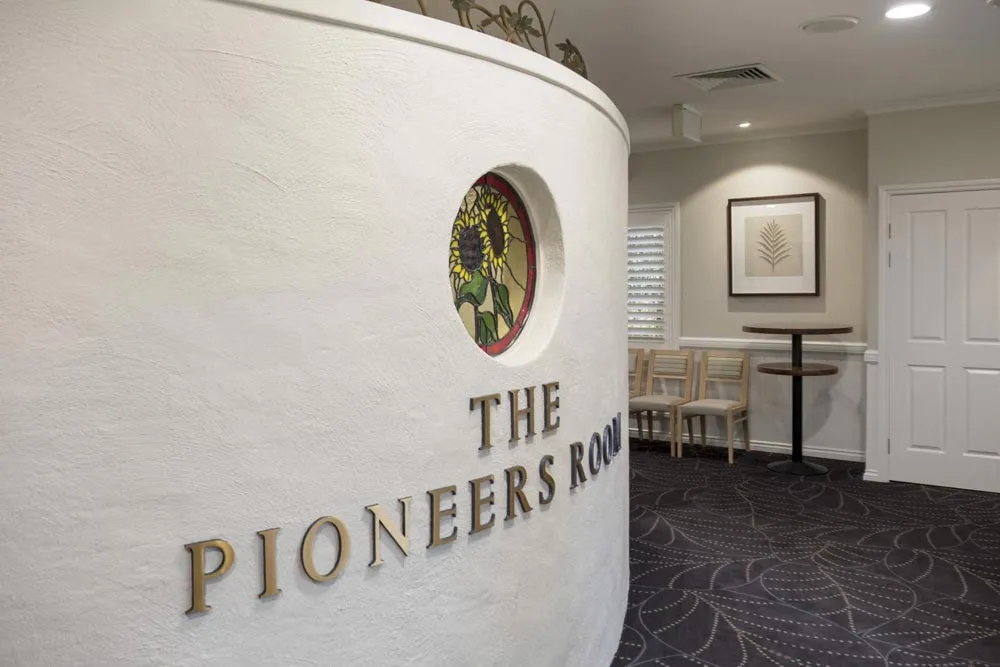 White curved wall reading "THE PIONEERS ROOM" at the entrance to an elegant indoor lounge.