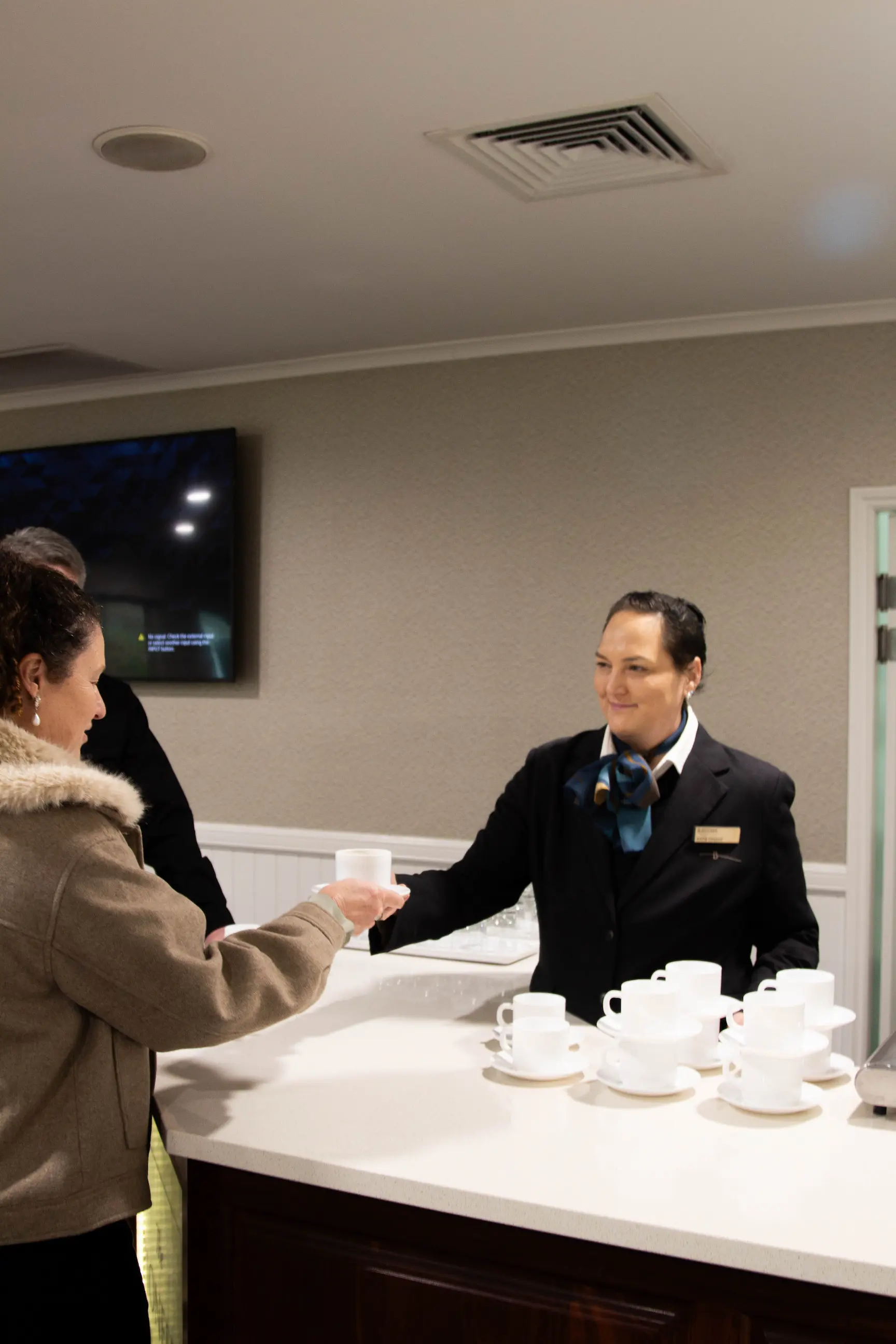 Staff member behind a wooden service counter handing a coffee cup to a guest.