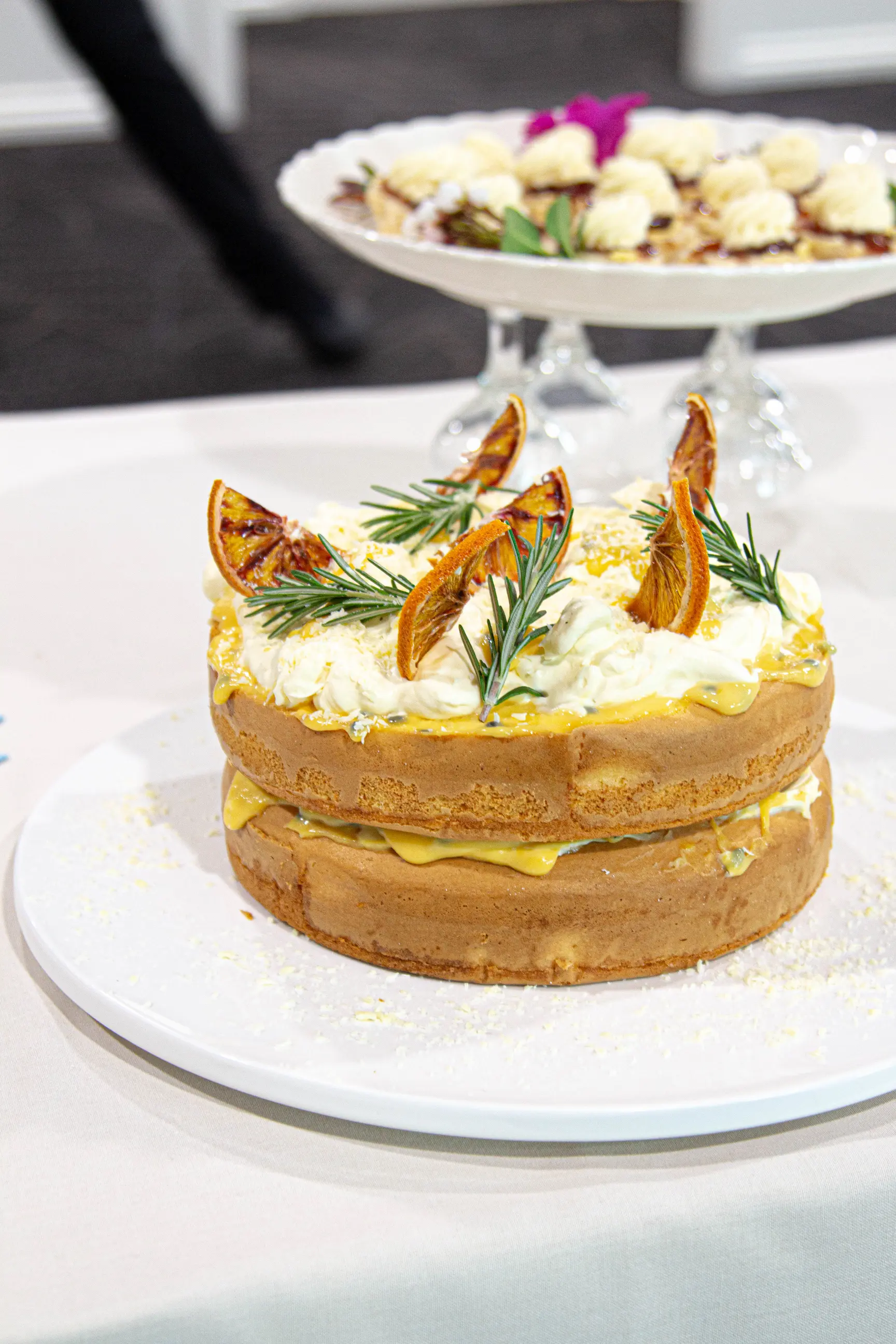Two-tier naked cake topped with white frosting and dried orange slices on a white plate.
