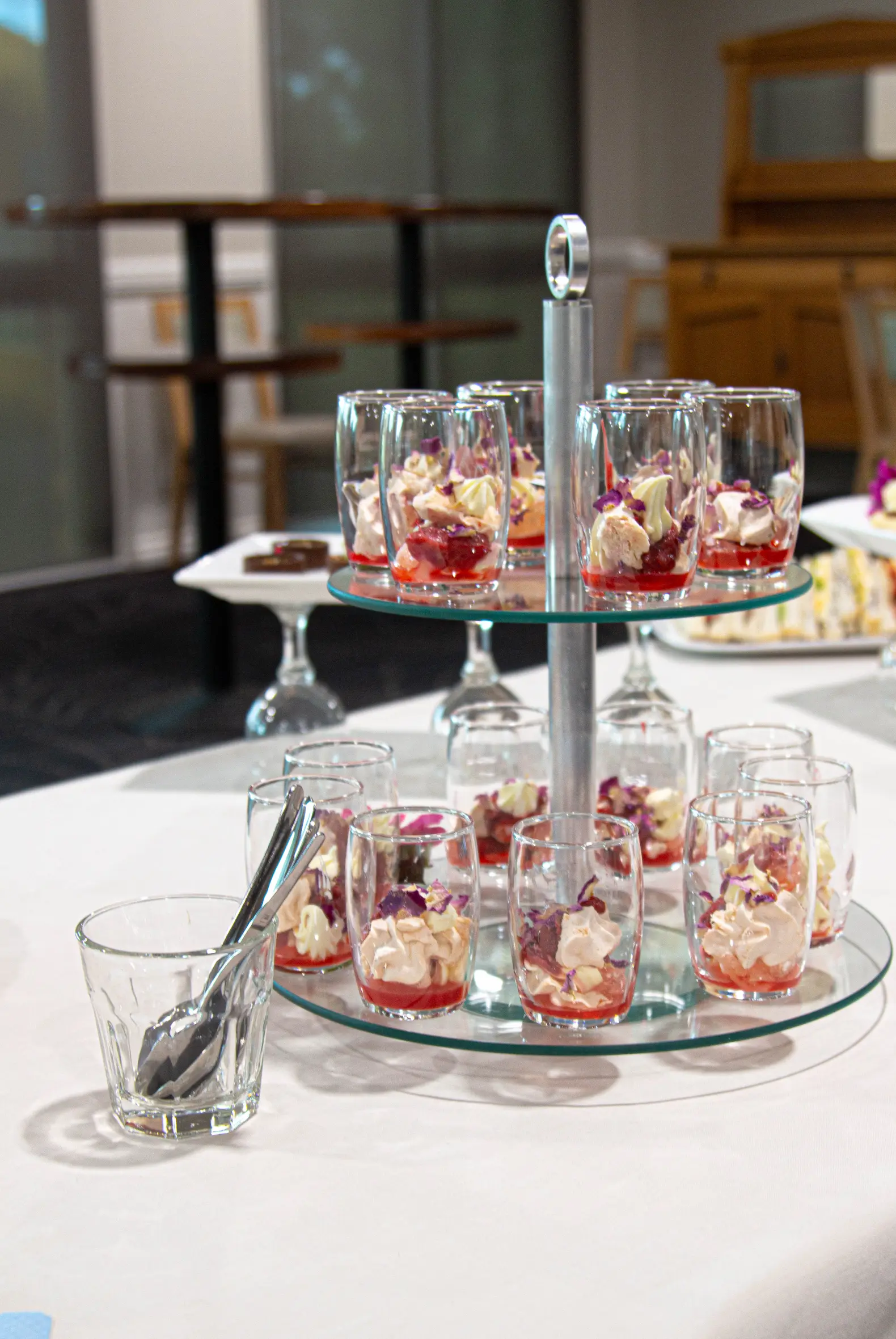 Two-tier glass stand displaying small parfait dessert cups on a catered table buffet.