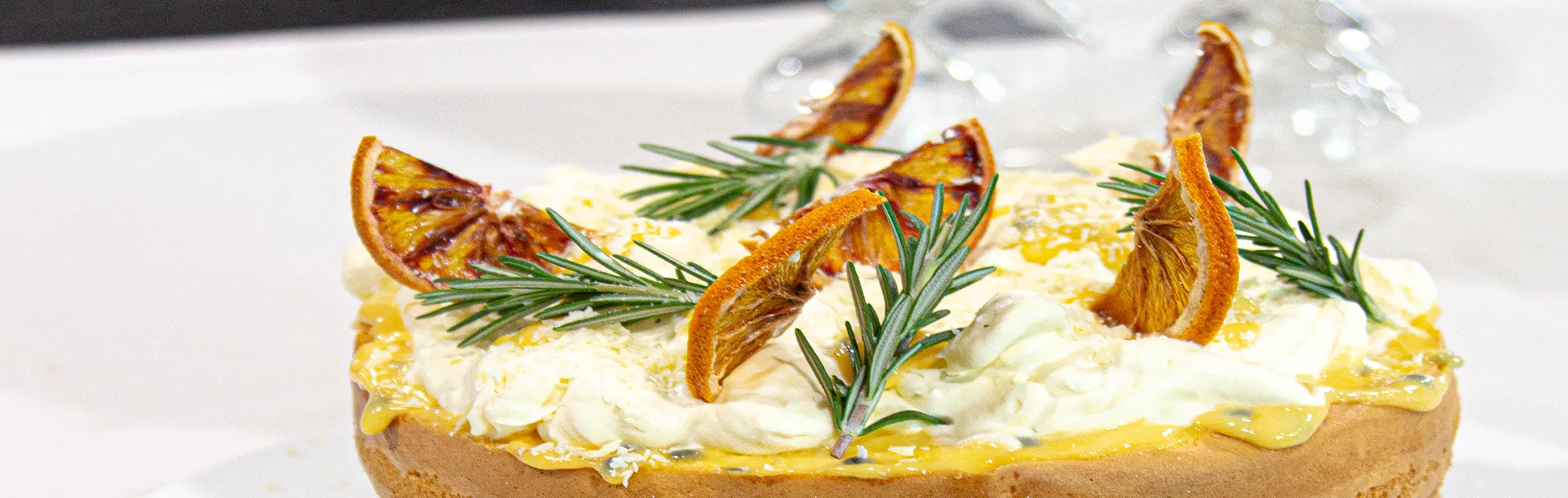 Gourmet citrus cake garnished with whipped cream, fresh rosemary, and dried orange slices.
