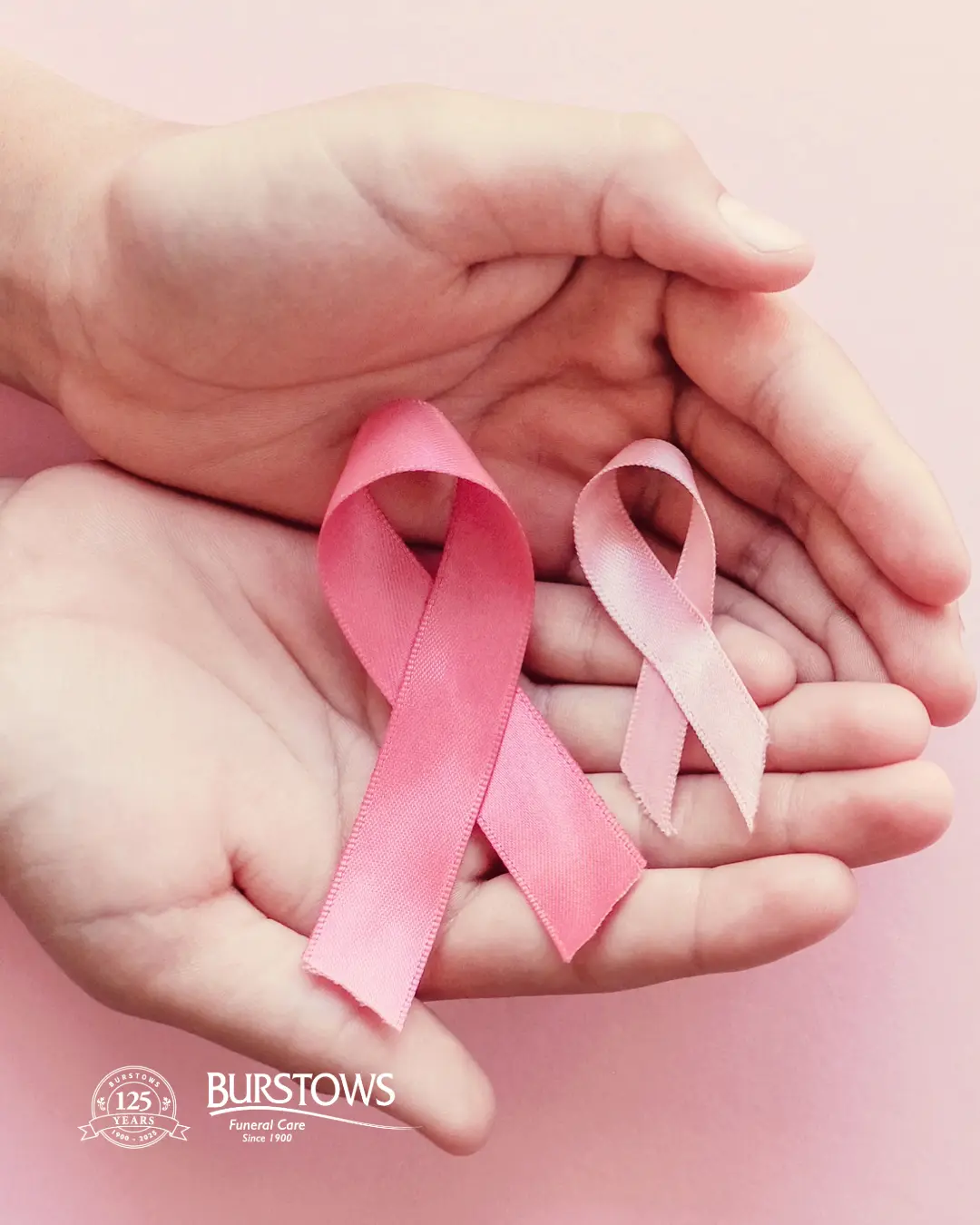 Two open hands gently holding a dark pink and a light pink breast cancer awareness ribbon against a soft pink background with the Burstows Funeral Care logo in the bottom corner.