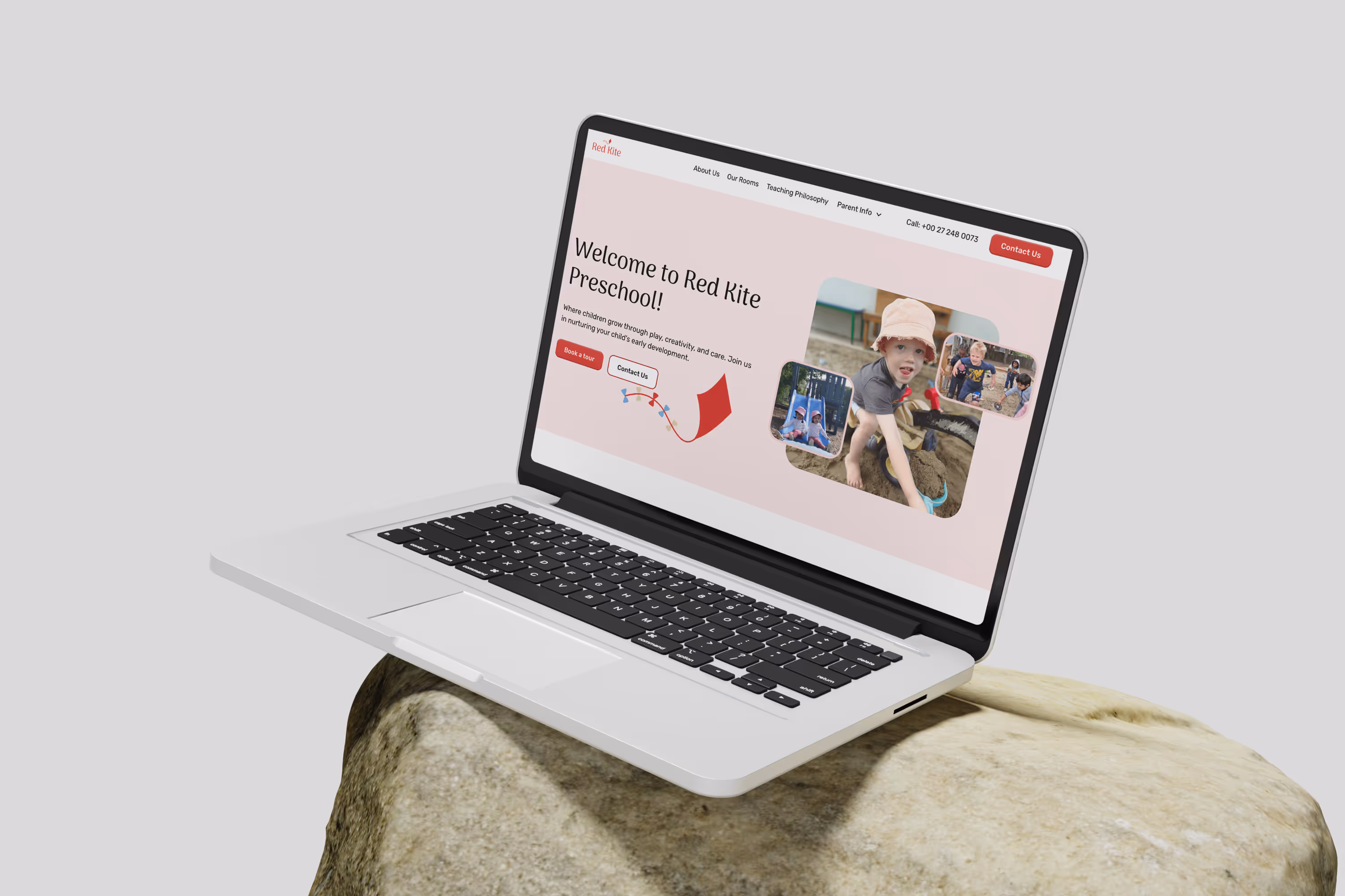 Laptop mockup on a light-colored rock, displaying a preschool website for Red Kite Preschool with a soft red and white color scheme, playful design, and images of happy children.