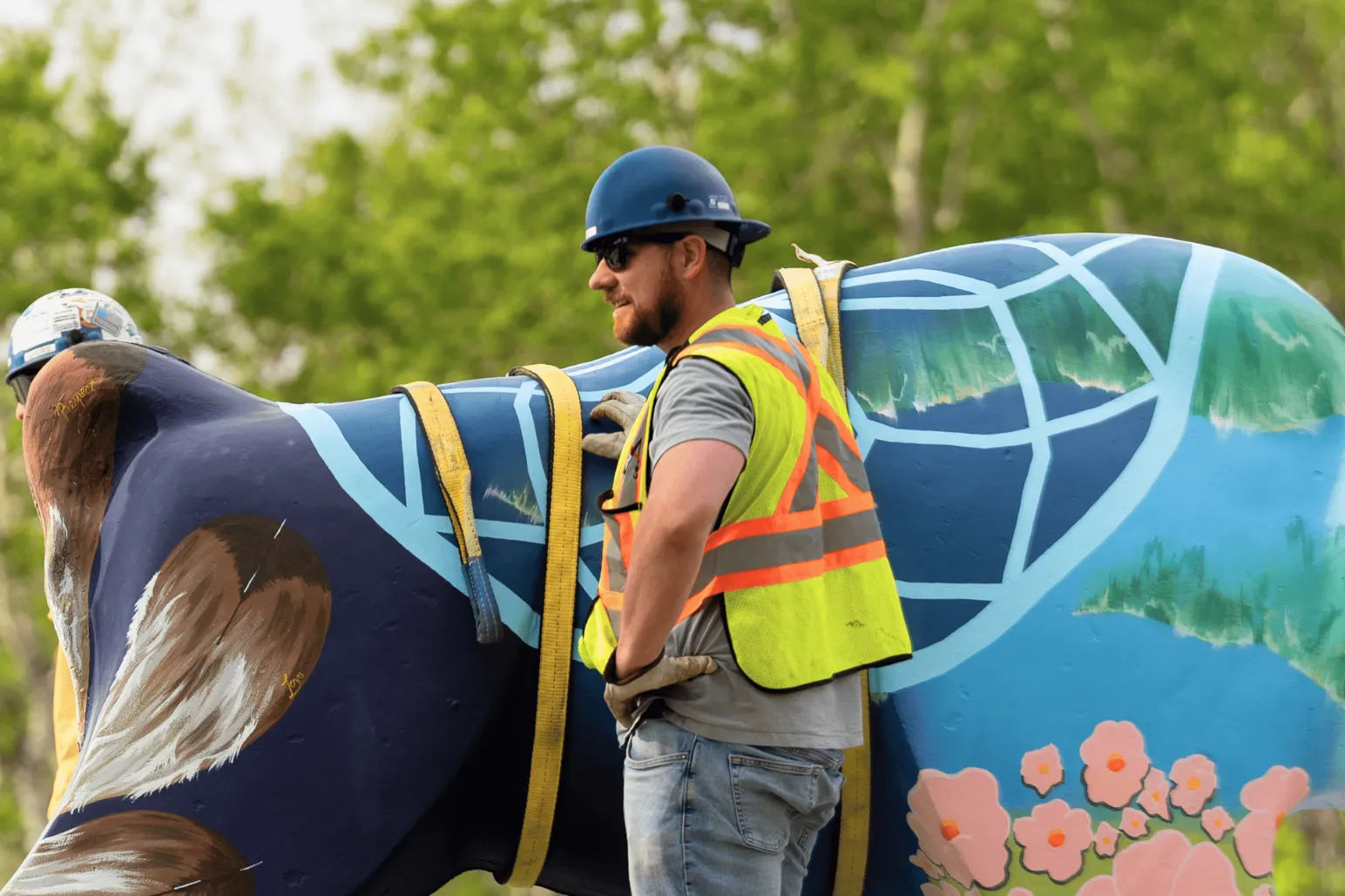 Worker adjusting rigging on blue bison public art sculpture during installation