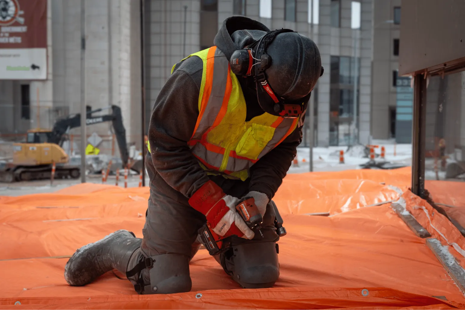Construction worker kneeling with cordless drill on orange protection tarp Portage and Main