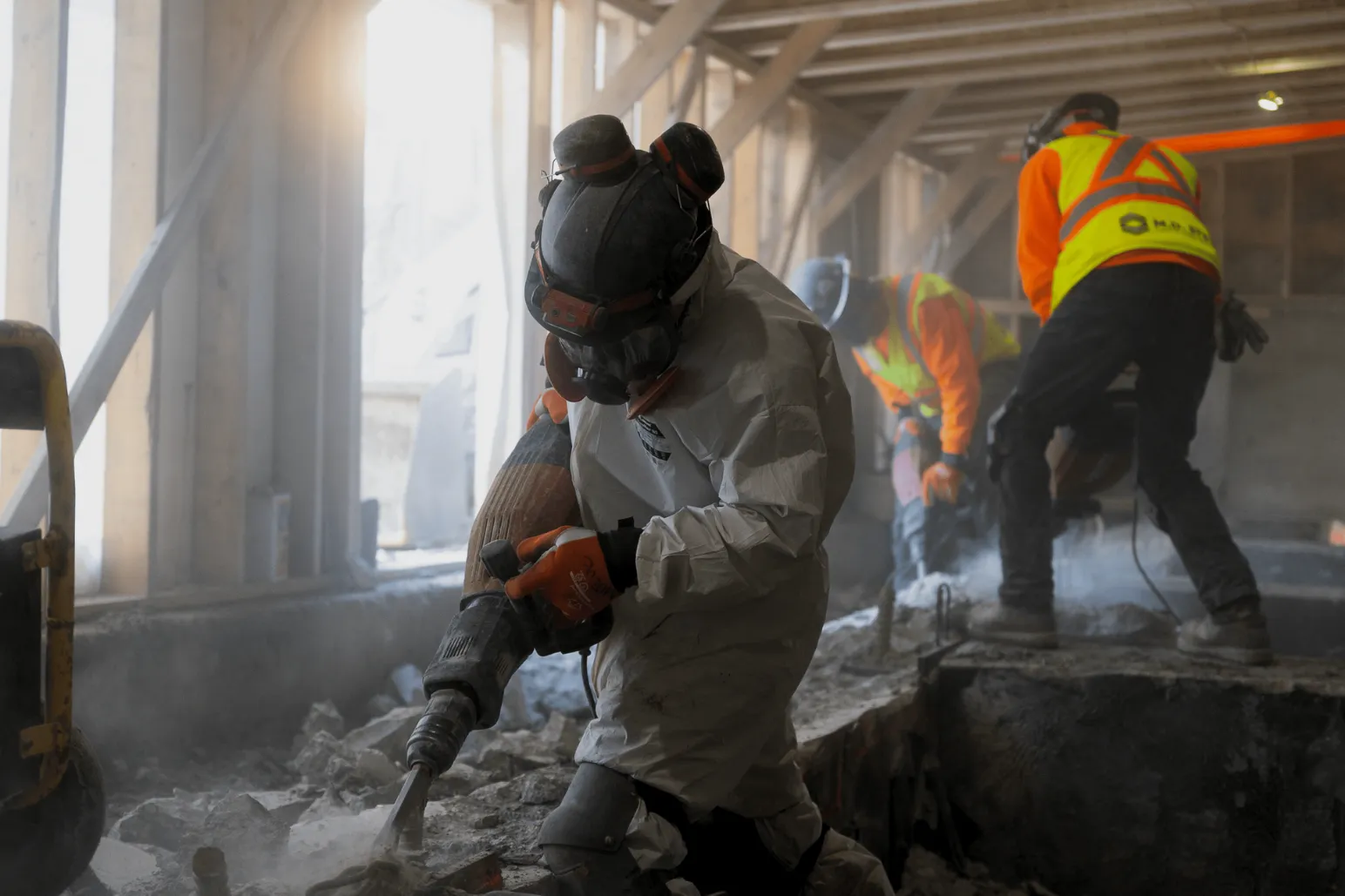 Construction worker using jackhammer breaking concrete in dusty underground workspace