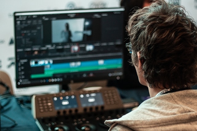 man, editor, color Over-the-shoulder view of a person working on video editing software, with a timeline interface visible on the computer monitor.correction