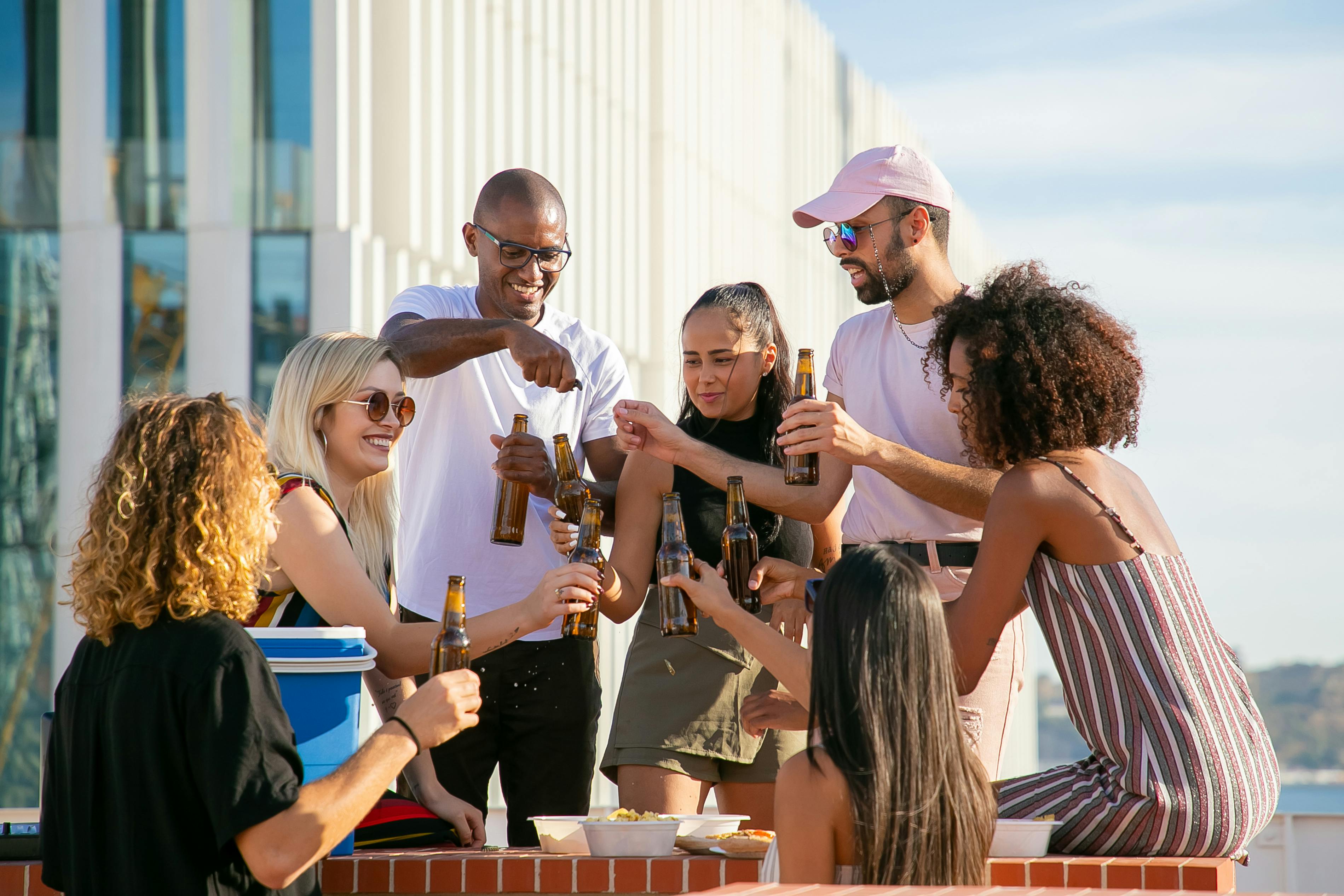 Happy friends clinking bottles on terrace