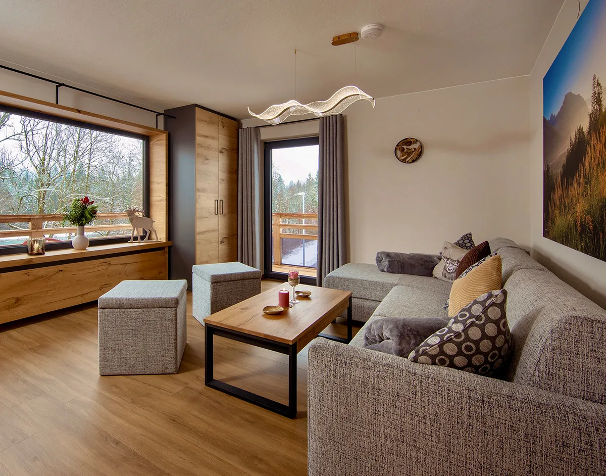 Modern living room with gray sectional sofa, wooden coffee table, cube ottomans, large window, and mountain landscape wall art.