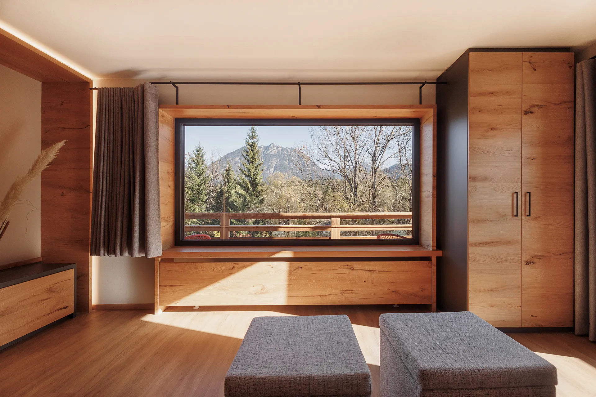 Minimalist room with wooden furniture and a large window showing a mountain and tree landscape.