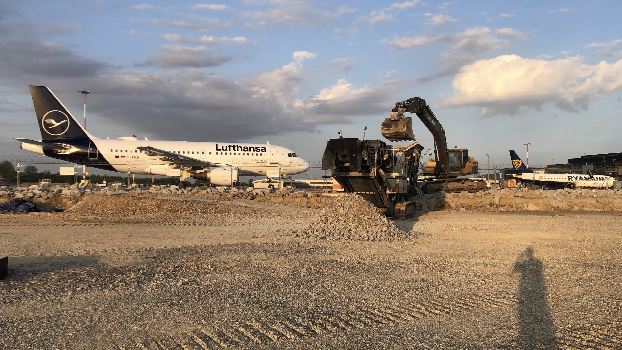 Lufthansa and Ryanair planes on runway near construction site with excavator moving gravel.