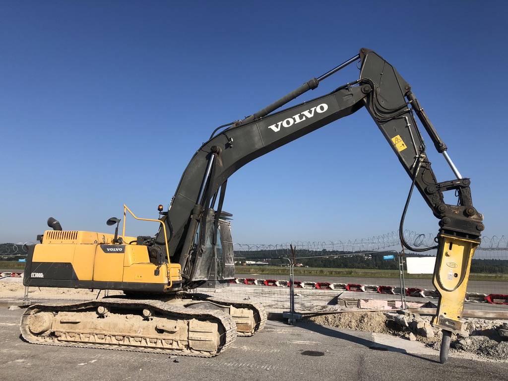 Yellow and black Volvo excavator with hydraulic hammer attachment on a construction site.