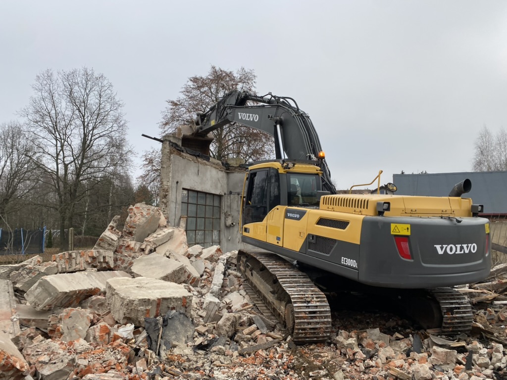 Yellow and black Volvo excavator demolishing a brick and concrete building with rubble around.