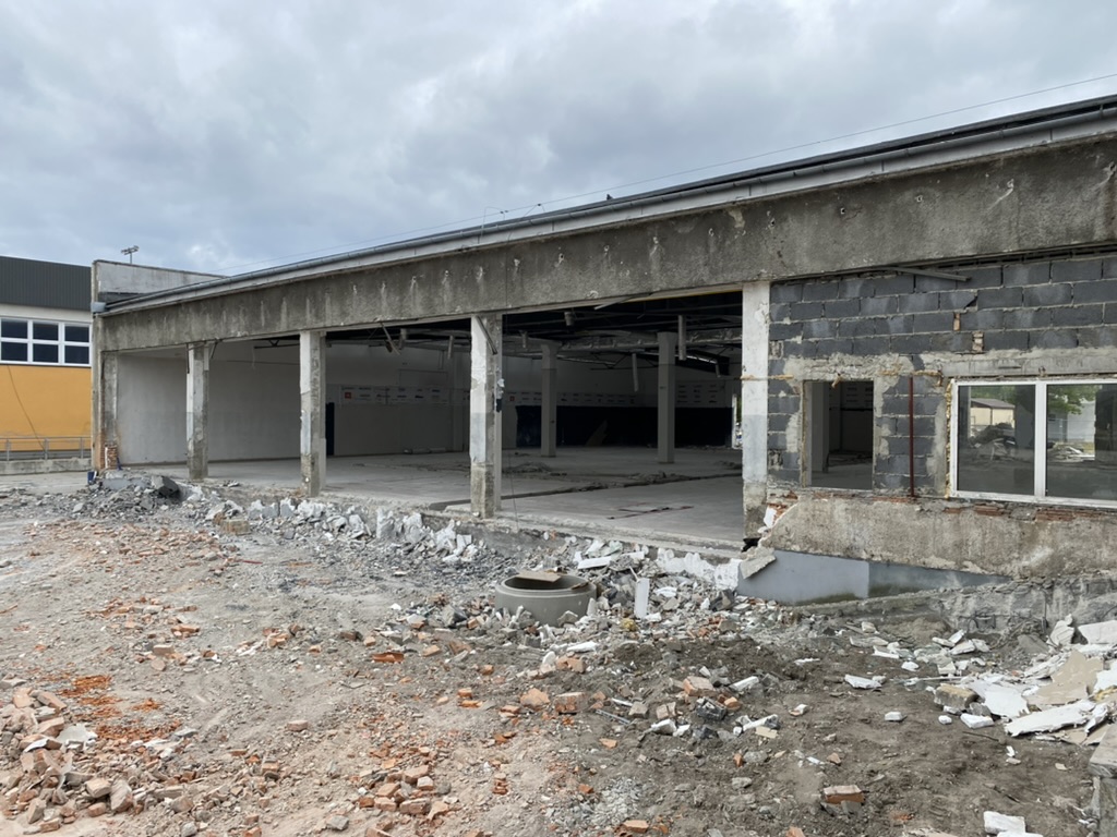 Partially demolished building with rubble and debris scattered around on cloudy day.
