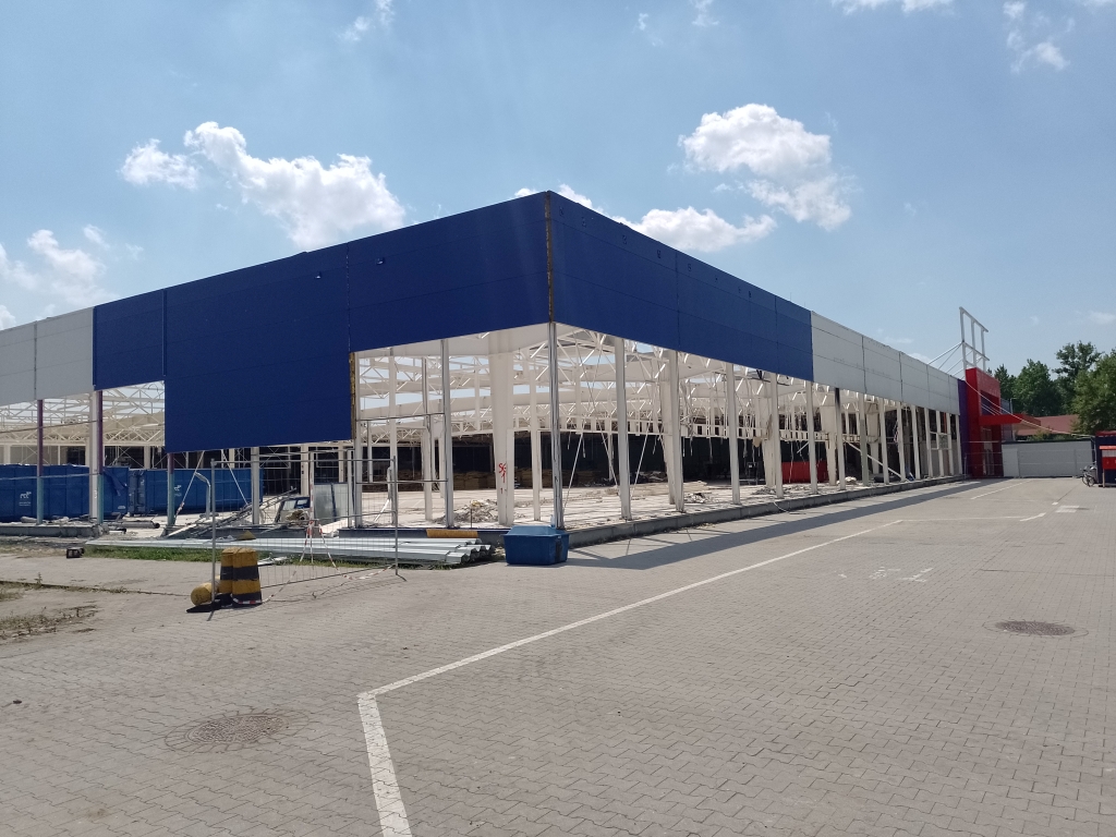 Partially constructed large building with blue and white panels and open framework under a sunny sky.