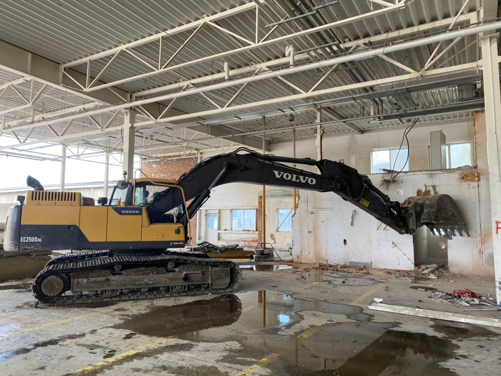 Yellow Volvo EC250D tracked excavator inside a partially demolished industrial building.