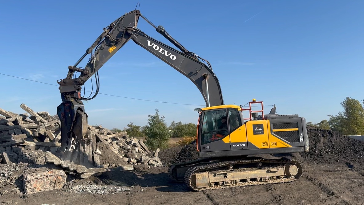 Yellow and black Volvo excavator breaking concrete rubble with hydraulic attachment on dirt site.