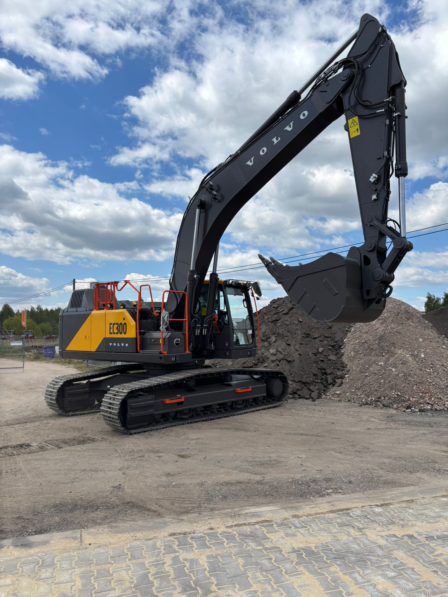 Volvo EC300 excavator with raised arm and bucket on a construction site with dirt piles.