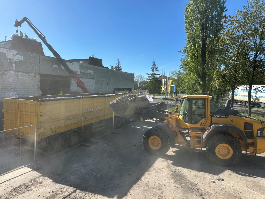 Yellow Volvo construction loader dumping rubble into a yellow trailer truck under clear blue sky.