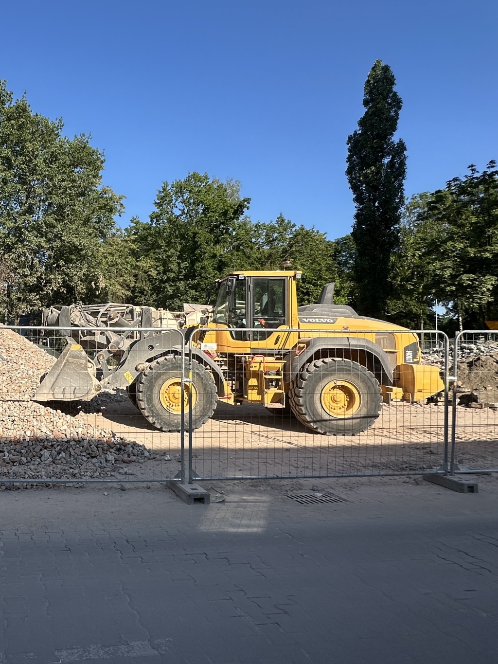Yellow Volvo wheel loader parked at construction site behind metal fencing on a sunny day.