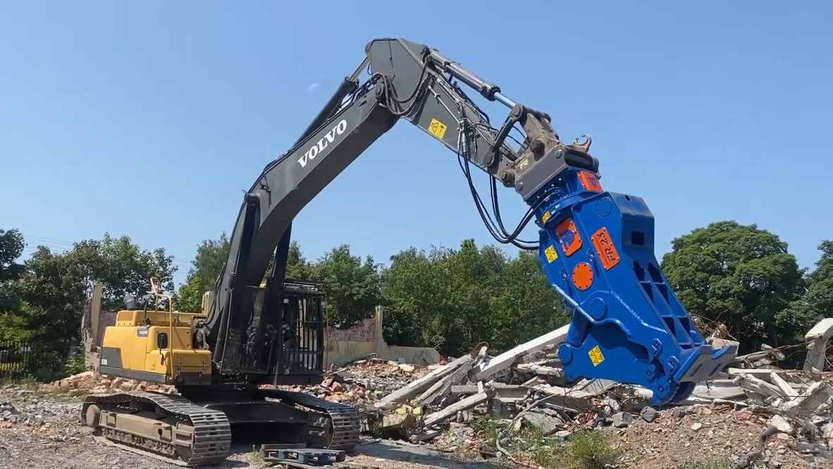 Volvo excavator with a blue hydraulic demolition attachment working on rubble under clear sky.