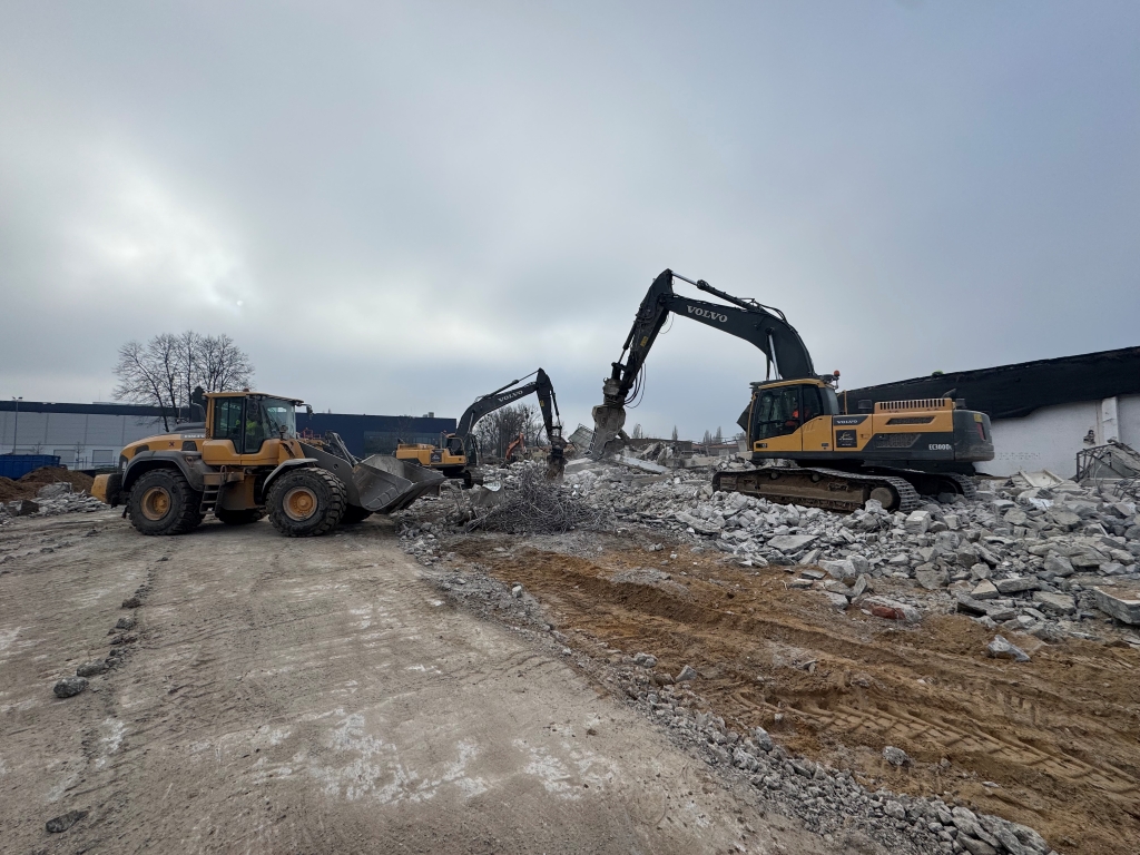 Construction site with two Volvo excavators and a loader amid rubble under cloudy sky.