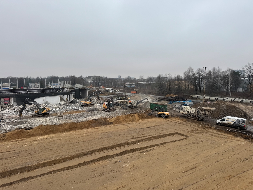 Construction site with excavators tearing down a building and earthmoving vehicles on cleared land.