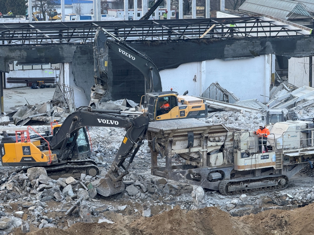 Construction site with Volvo excavators and a worker operating heavy machinery among rubble.