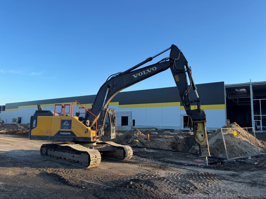 Yellow and black Volvo excavator with a hydraulic breaker attachment at a construction site.