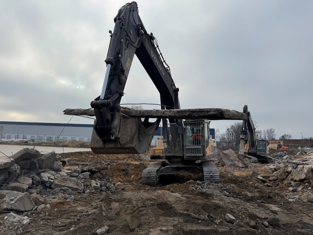 Two excavators digging in a rocky construction site under a cloudy sky.