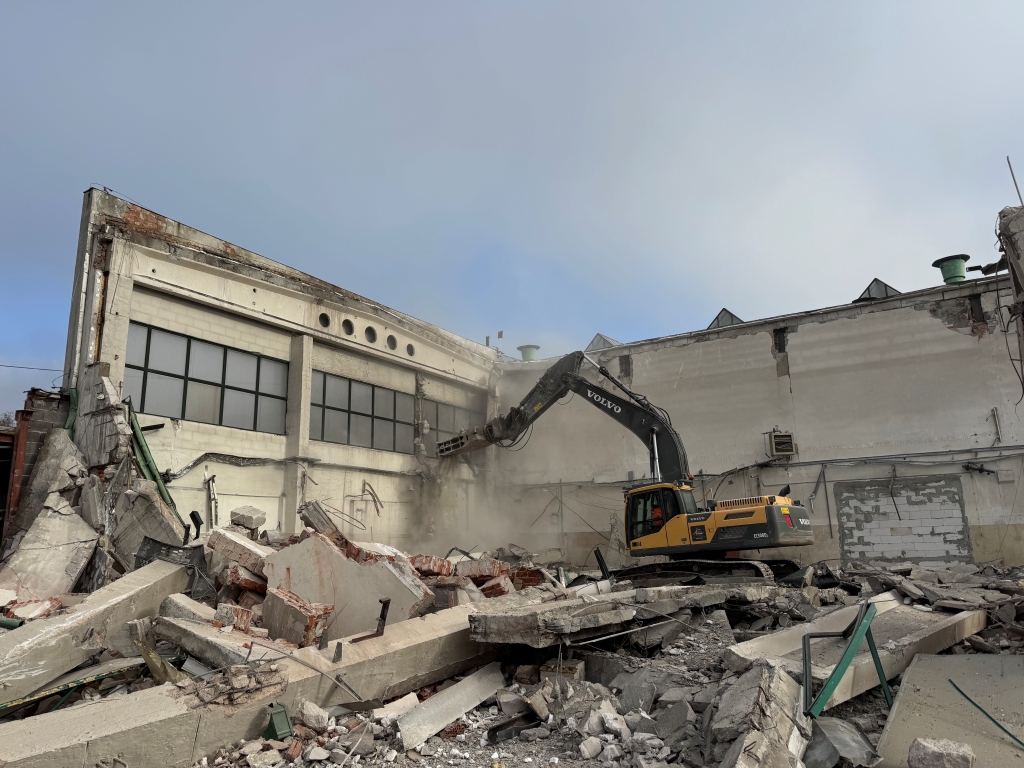 Yellow Volvo excavator demolishing a building with rubble and debris scattered around.