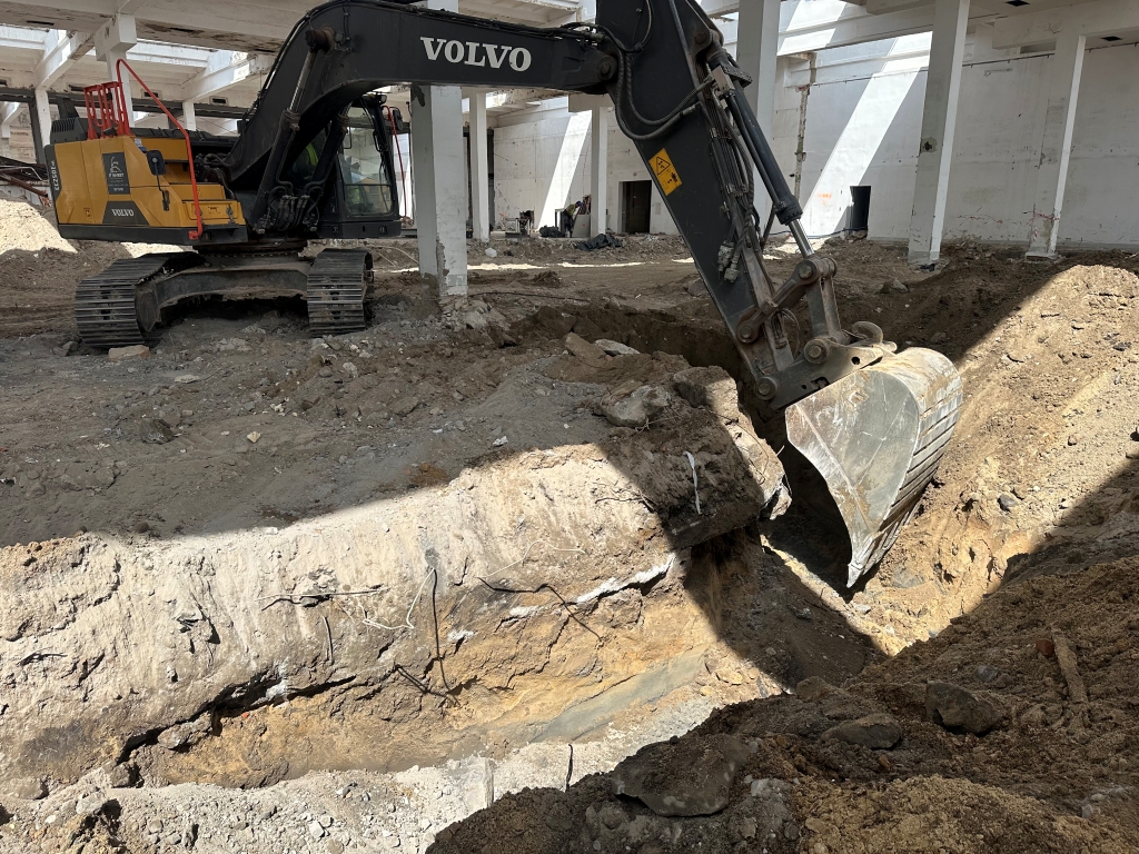 Volvo excavator digging a large trench inside a building under construction or renovation.