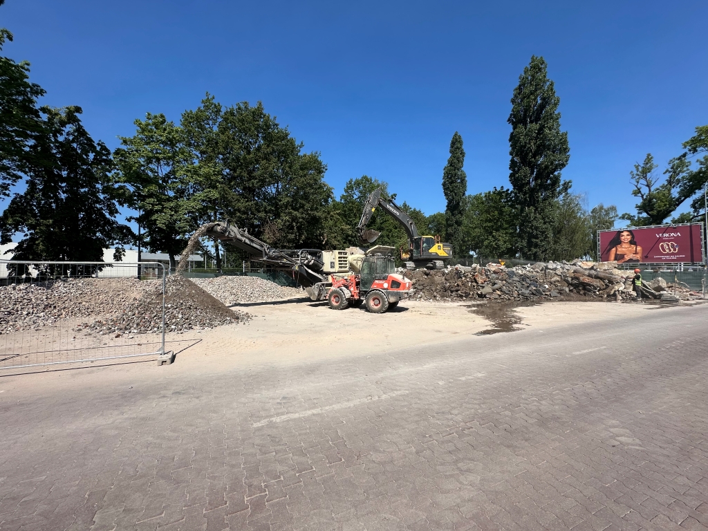 Construction site with machinery sorting rubble and a worker near a large pile of stones under clear blue sky.